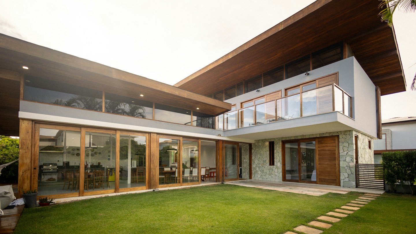 Rumah modern dengan pintu kaca dan aksen kayu menghadap halaman rumput.